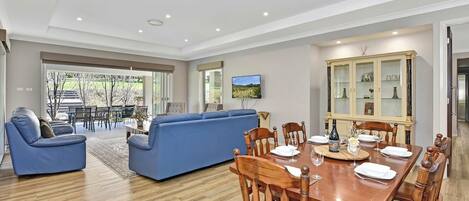 A modern living room with a blue sofa, dining table set for six, and a large cabinet with glass doors.
