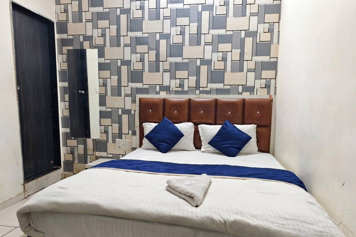 A neatly made bed with a brown headboard, white bedding, and blue pillows.