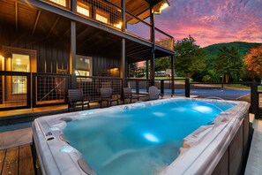 Un jacuzzi con terraza de madera y sillas, un área de estar al aire libre cubierta y vistas a la montaña.
