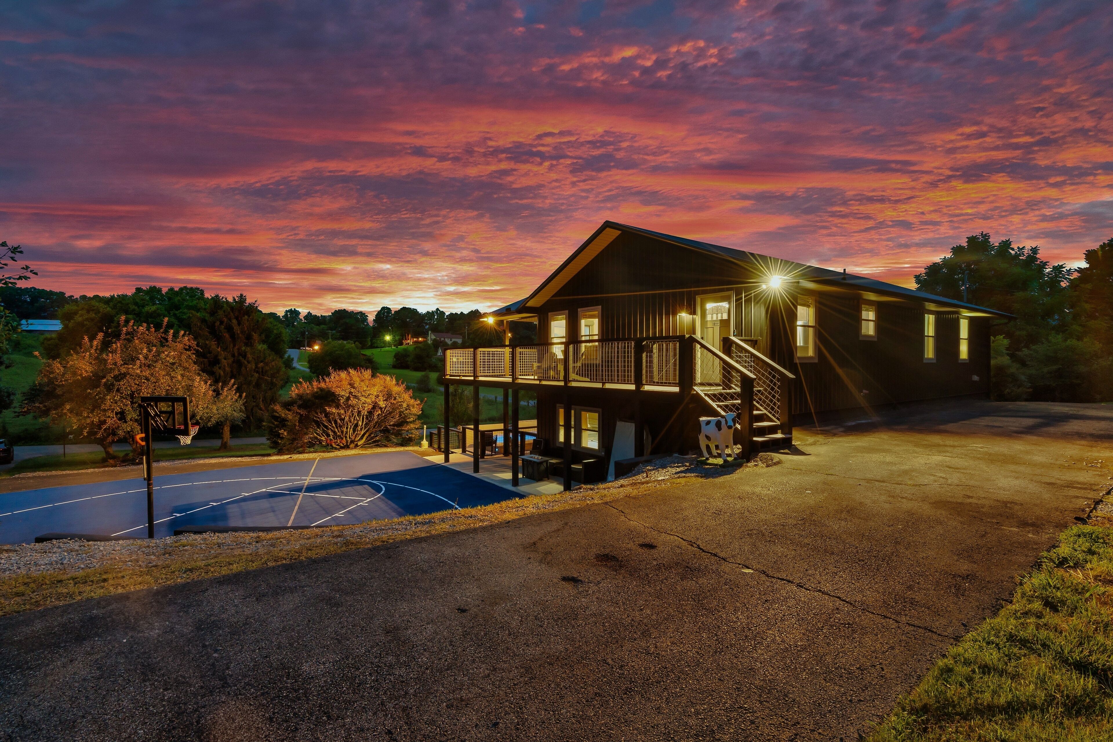 A two-story house with a balcony, a basketball court, and a driveway.