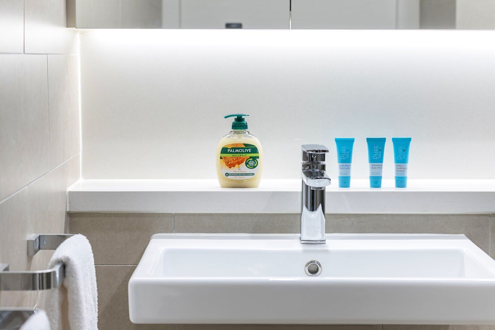 A bathroom sink with a chrome faucet, a bottle of Palmolive soap, and three tubes of Pure Body Body Wash on the countertop.