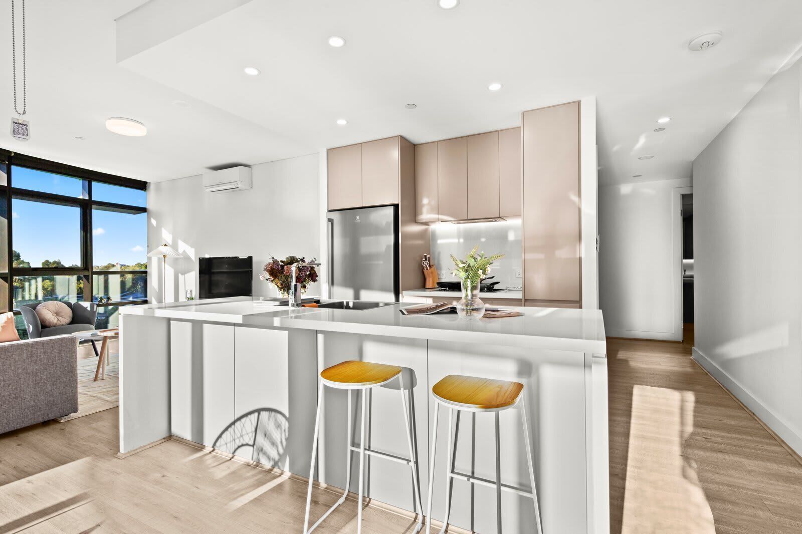 A modern kitchen with a central island, bar stools, and a view of the outdoors.