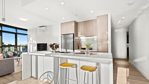 A modern kitchen with a central island, bar stools, and a view of the outdoors.