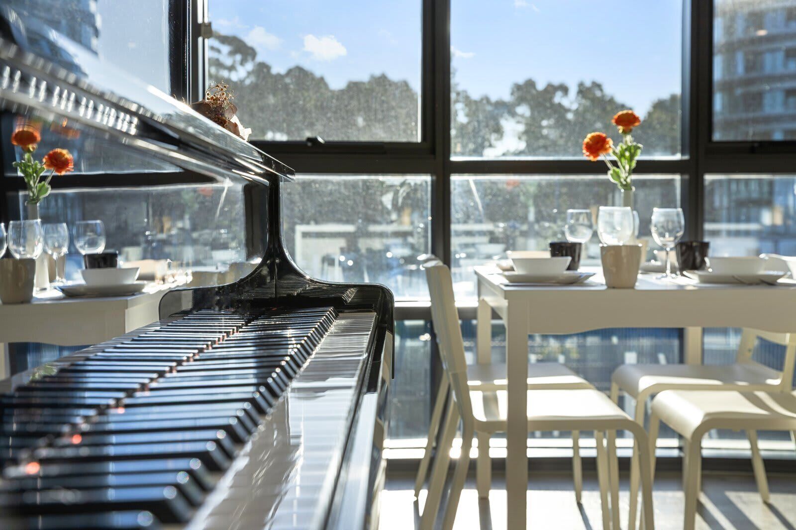 A piano in a dining area with a view of buildings through large windows.
