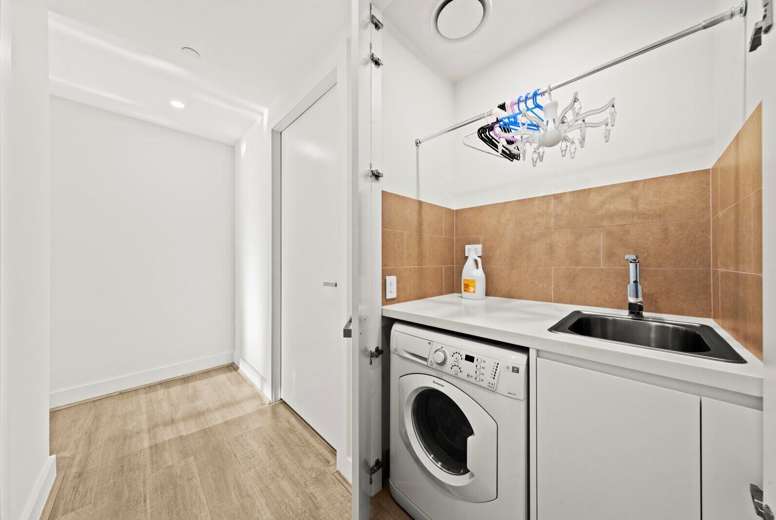 A compact laundry room with a washing machine, a sink, and a drying rack.