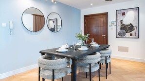 Un coin repas avec une table noire, six chaises grises à revêtement rembourré et un grand miroir au mur.