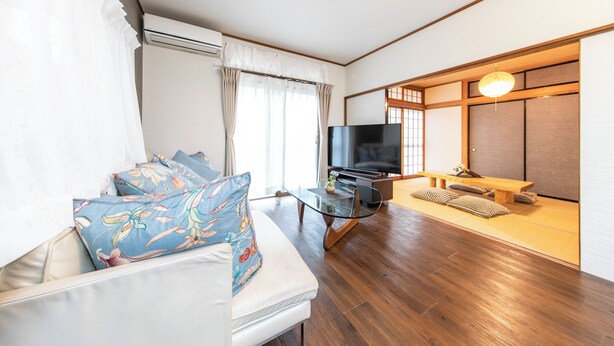 A modern living room with a sofa, TV, and a traditional Japanese-style room with tatami mats and a low table. - K&K HOUSE (Takasaki)