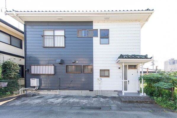 A two-story building with a dark grey and white facade, multiple windows, and a small porch area. - K&K HOUSE (Takasaki)