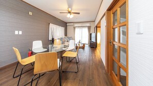 A modern room with a glass dining table, wooden chairs, a ceiling fan, and a television. - K&K HOUSE (Takasaki)