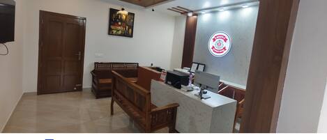 Un área de recepción con un banco de madera, un mostrador con una computadora y un letrero en la pared.