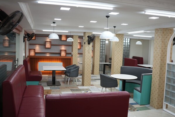 A modern restaurant with red seating, white tables, and pendant lighting. - Benzy Tourist Home (Ponnani)