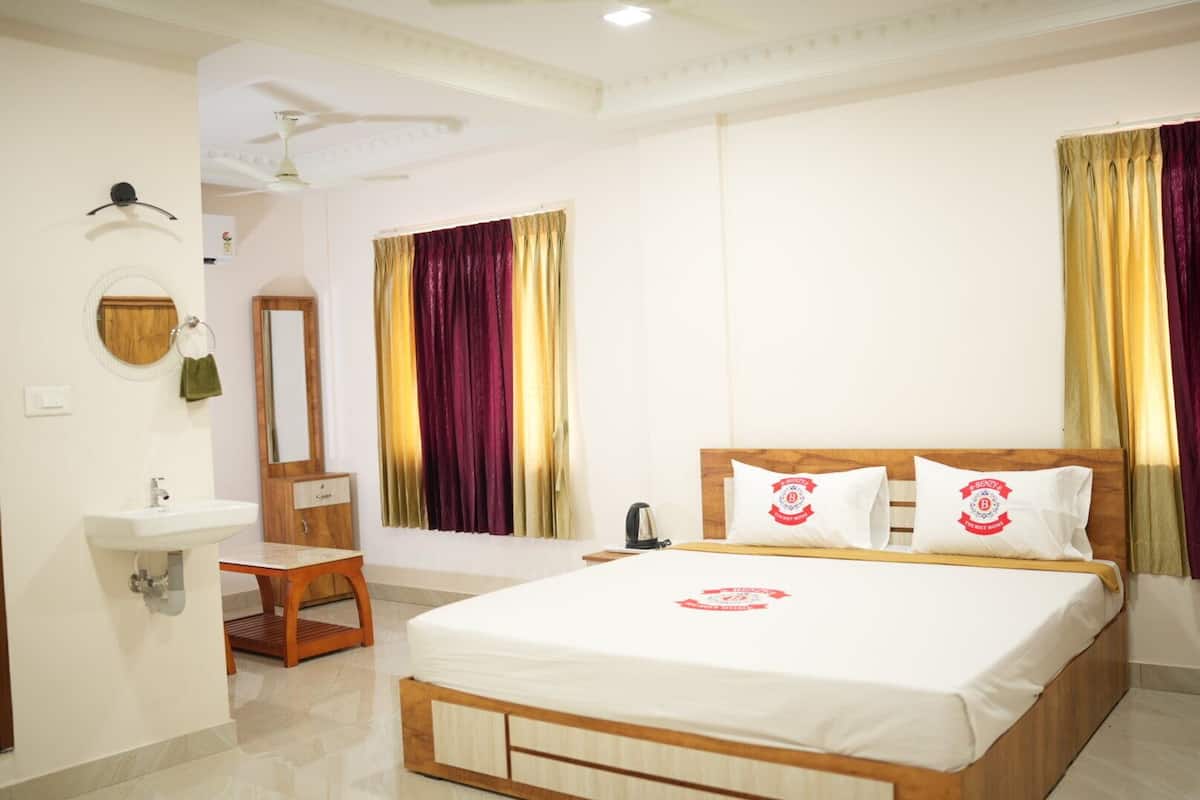 Una habitación de hotel con una cama grande, un cabecero de madera, una mesita de noche, un espejo, un lavabo y una ventana con cortinas.