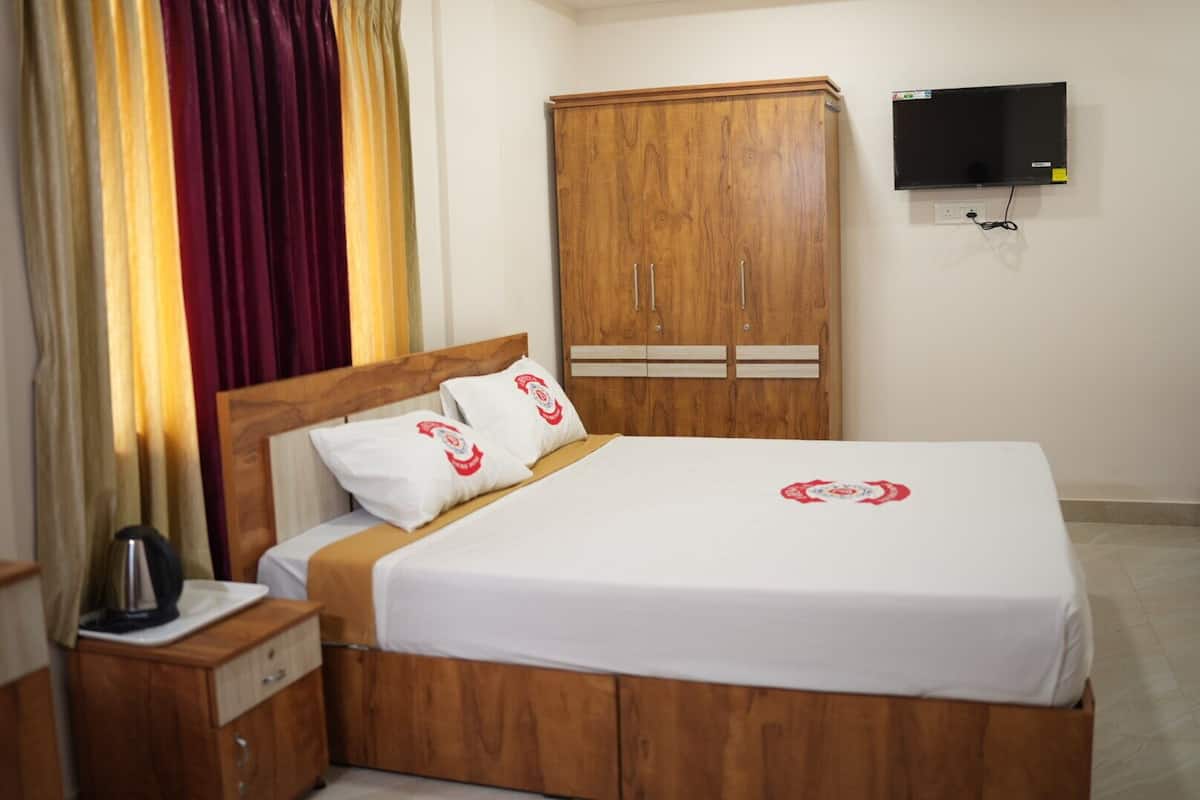 Habitación de hotel con cama de madera, ropa de cama blanca, armario de madera, televisor de pantalla plana en la pared y mesita de noche con hervidor.