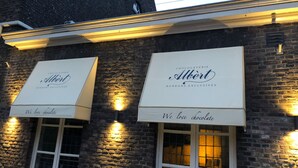 Eine Gebäudefassade mit zwei Markisen, auf denen der Name 'Albert' und der Schriftzug 'Wir lieben Schokolade' stehen.