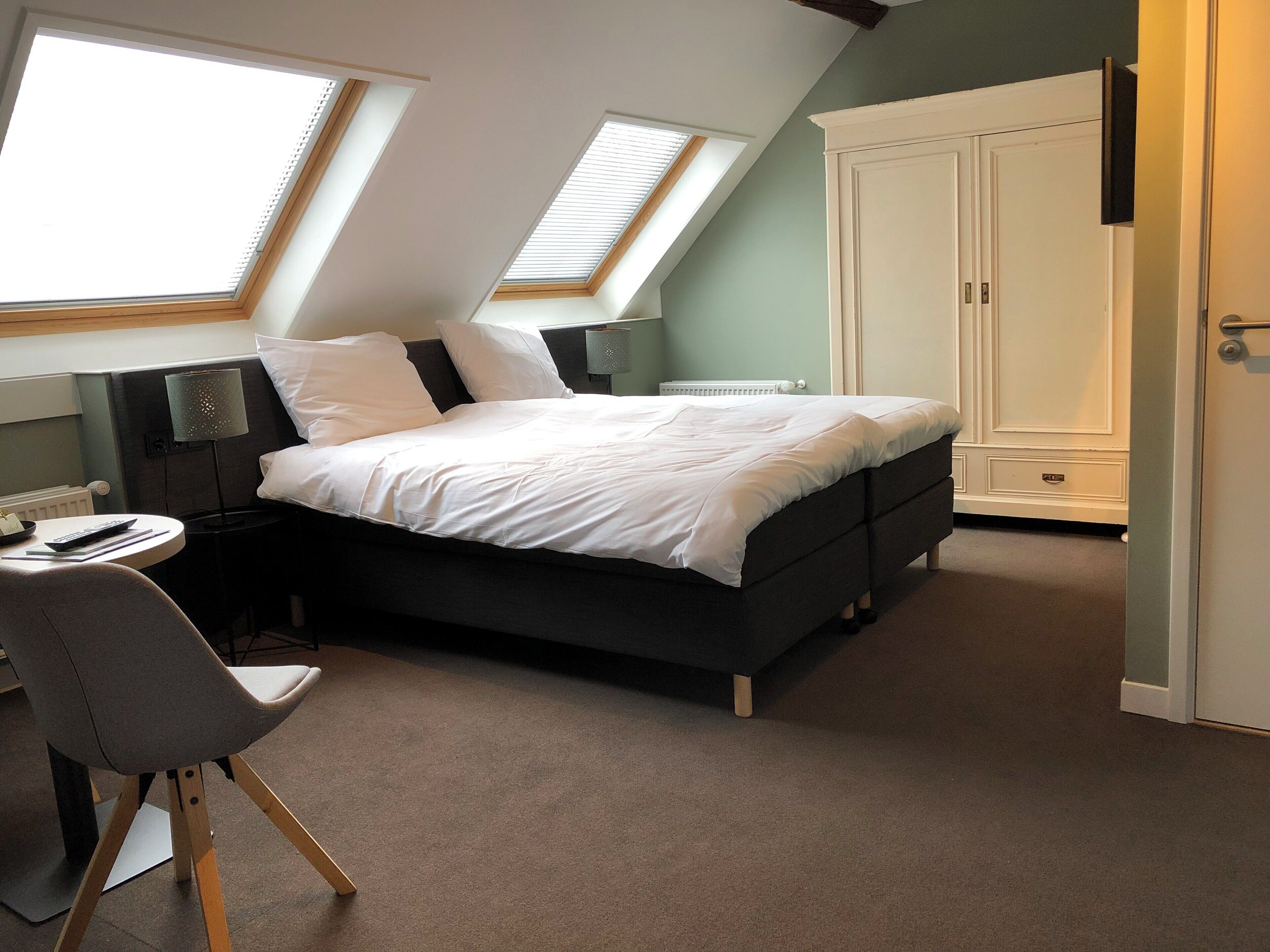 A bedroom with a bed, a desk, and a chair. There are skylights and a wardrobe.