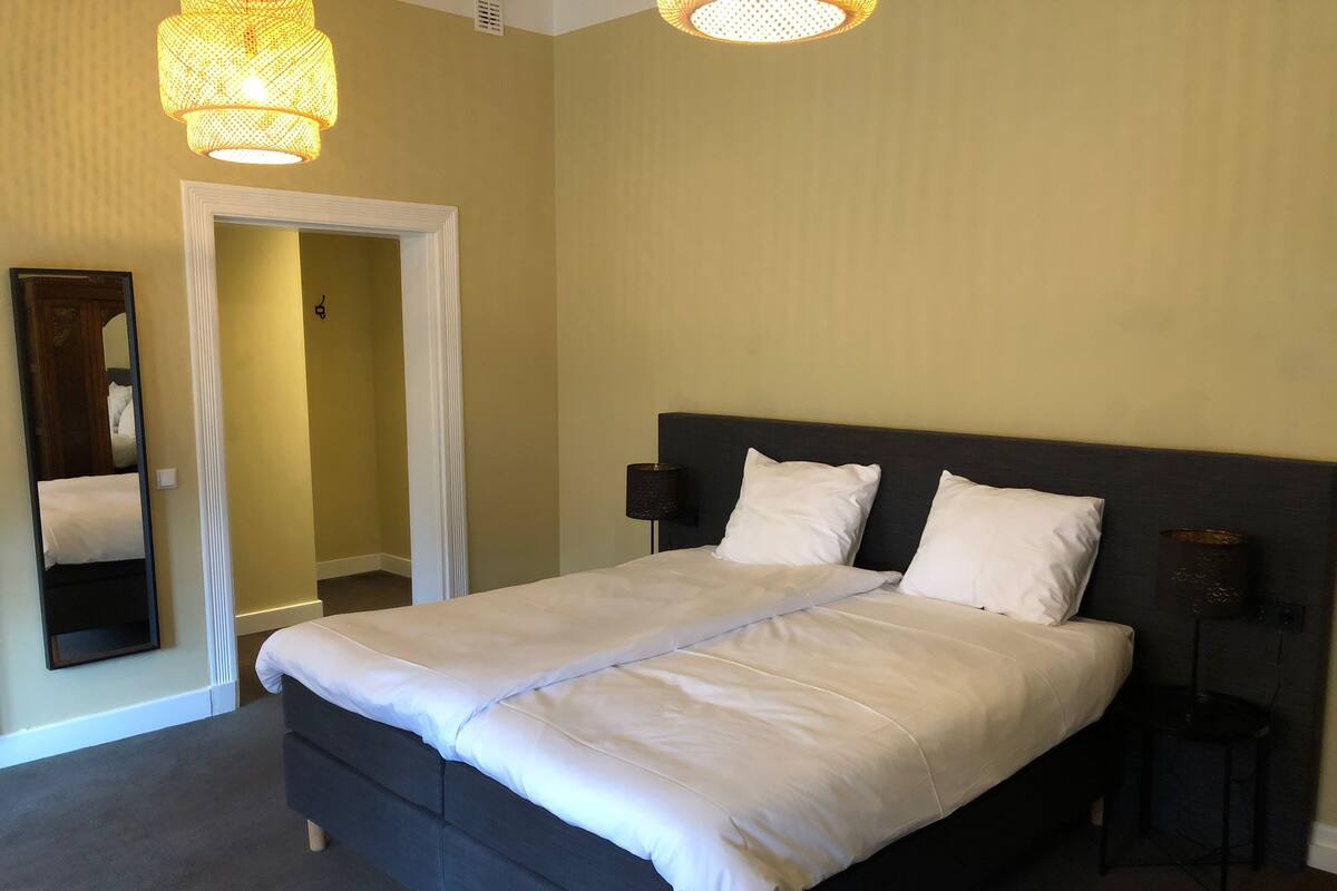 Un dormitorio con una cama, un espejo, una puerta y dos lámparas fijadas a la pared.