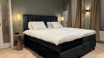 A modern bedroom with a large bed, two bedside lamps, and a small wooden side table.