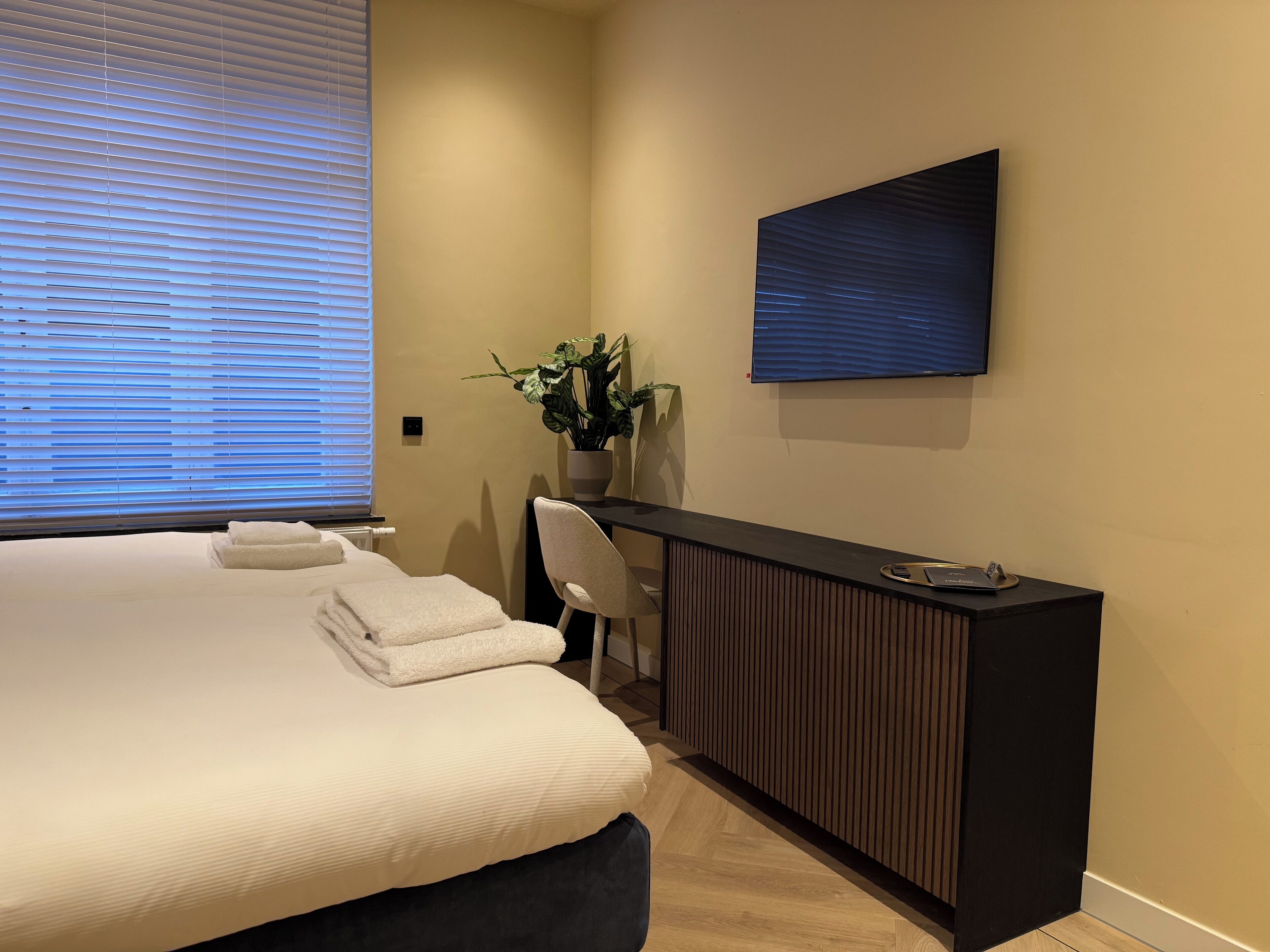 A modern hotel room with a large bed, a desk, and a potted plant.