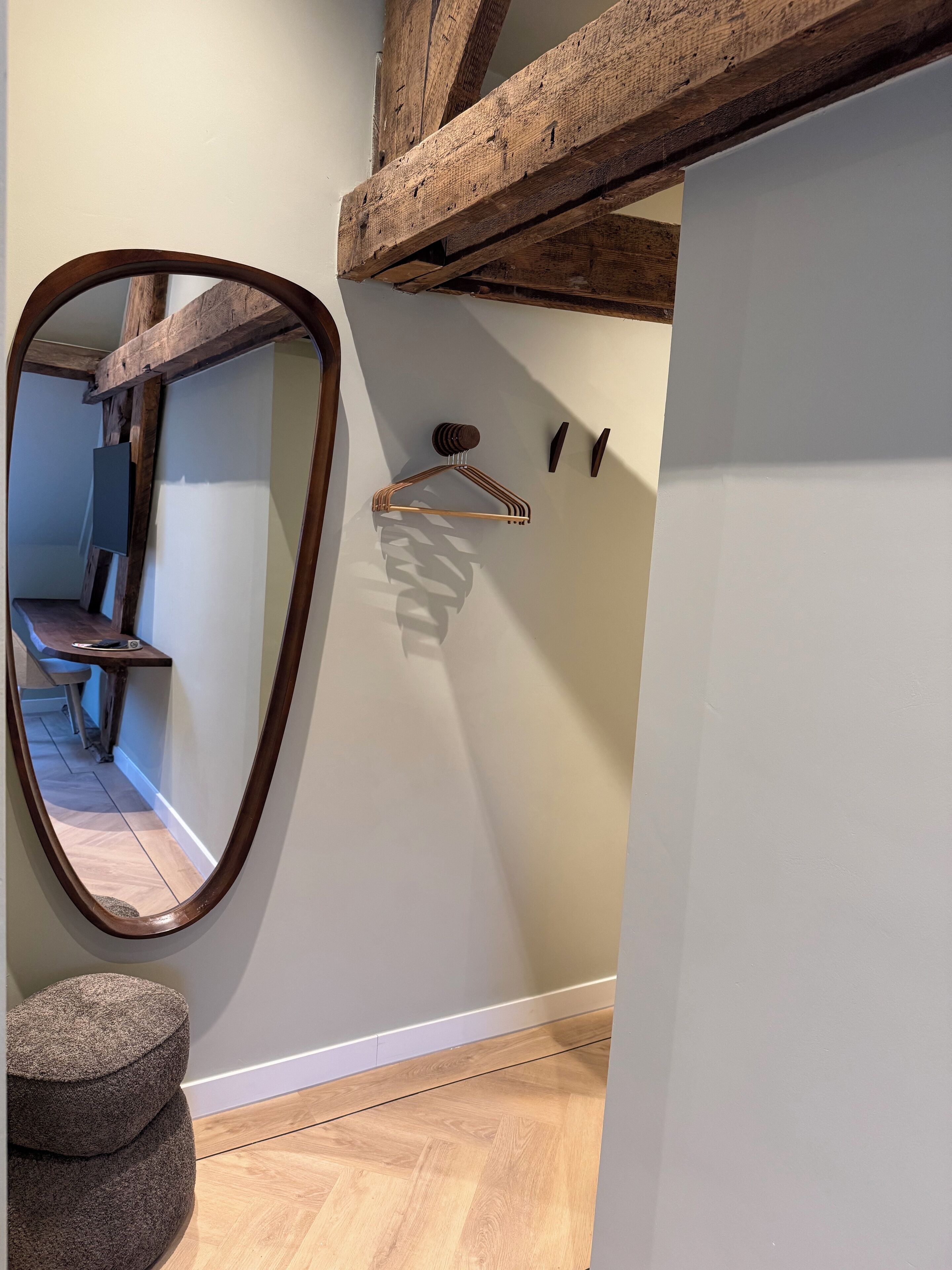 A room with a wooden ceiling beam, a mirror, a stool, and a wall-mounted coat rack.