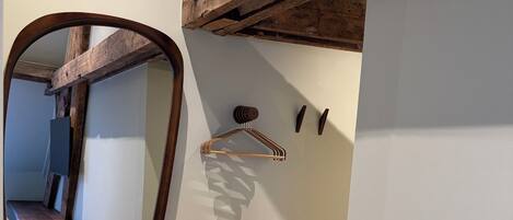 Una stanza con trave in legno al soffitto, uno specchio, uno sgabello e un appendiabiti a parete.