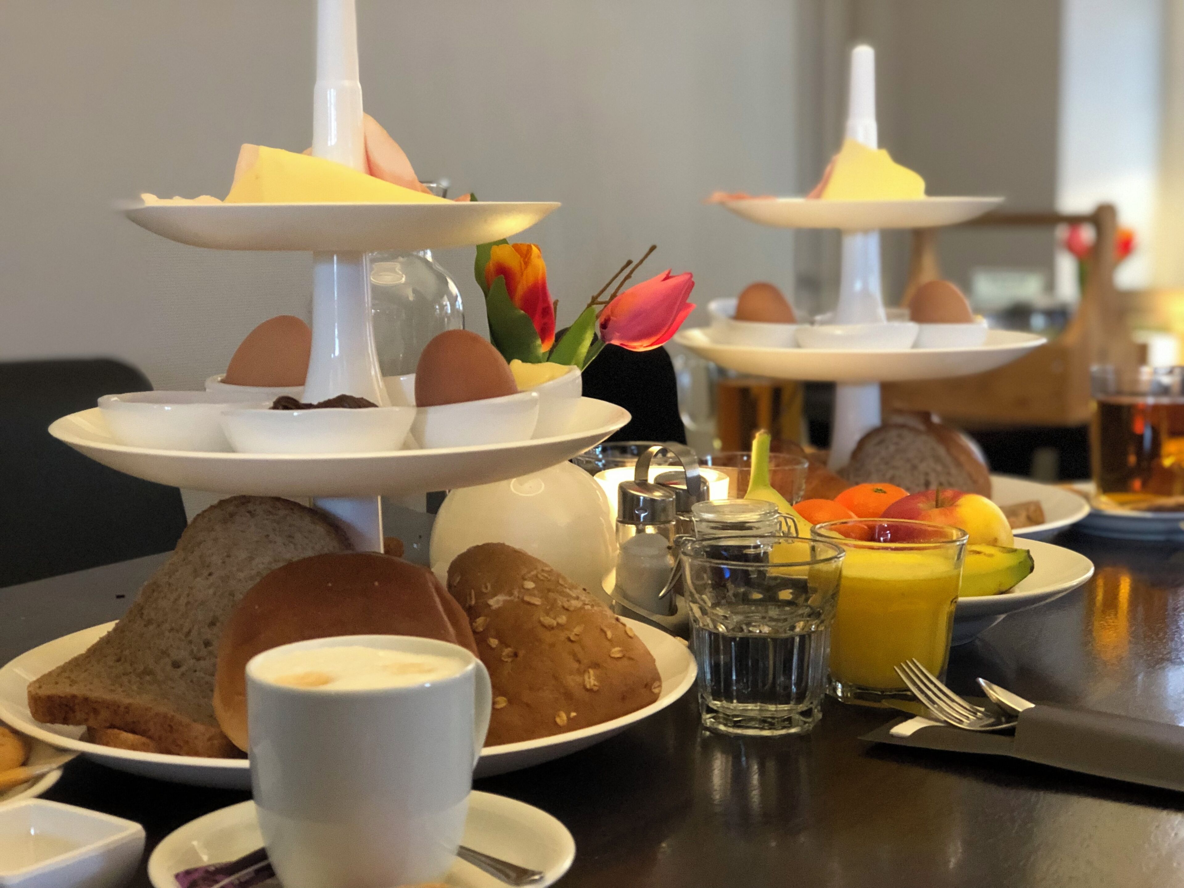 Impostazione colazione con diverse porzioni di uova, pane e dolci, insieme a una tazza di caffè e un bicchiere di succo d'arancia.