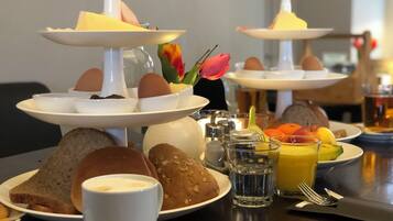 Impostazione colazione con diverse porzioni di uova, pane e dolci, insieme a una tazza di caffè e un bicchiere di succo d'arancia.