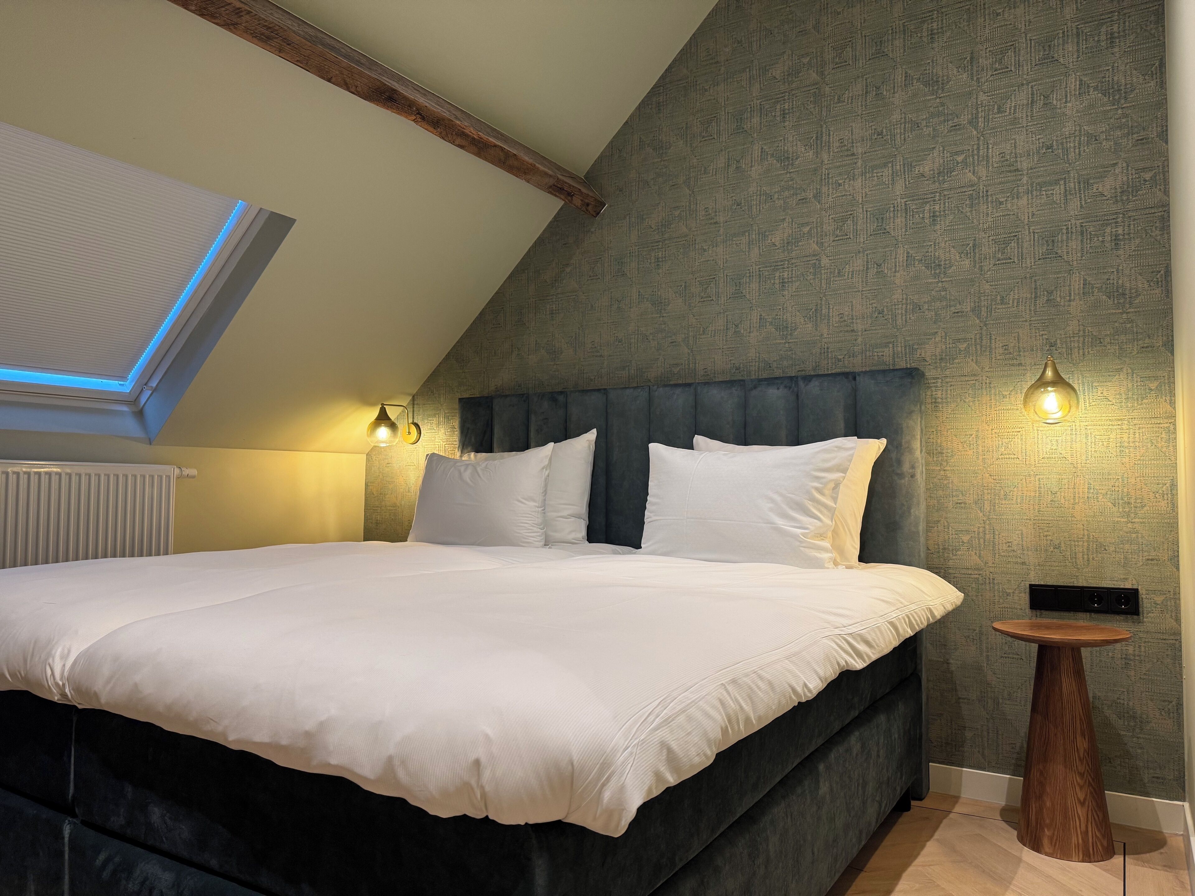 A bedroom with a large bed, a sloped ceiling, a radiator, and two wall-mounted lights.