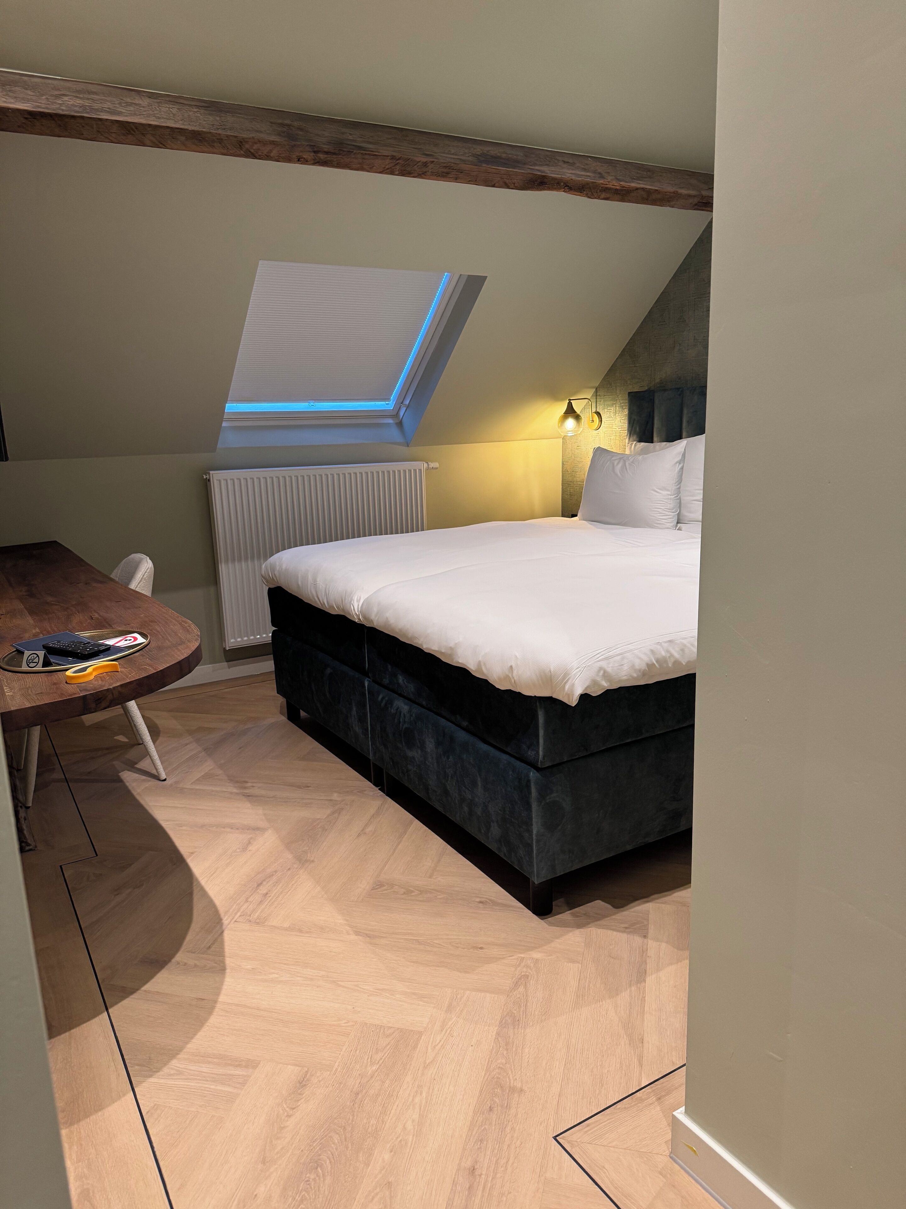 Un dormitorio con cama, escritorio, radiador y tragaluz.