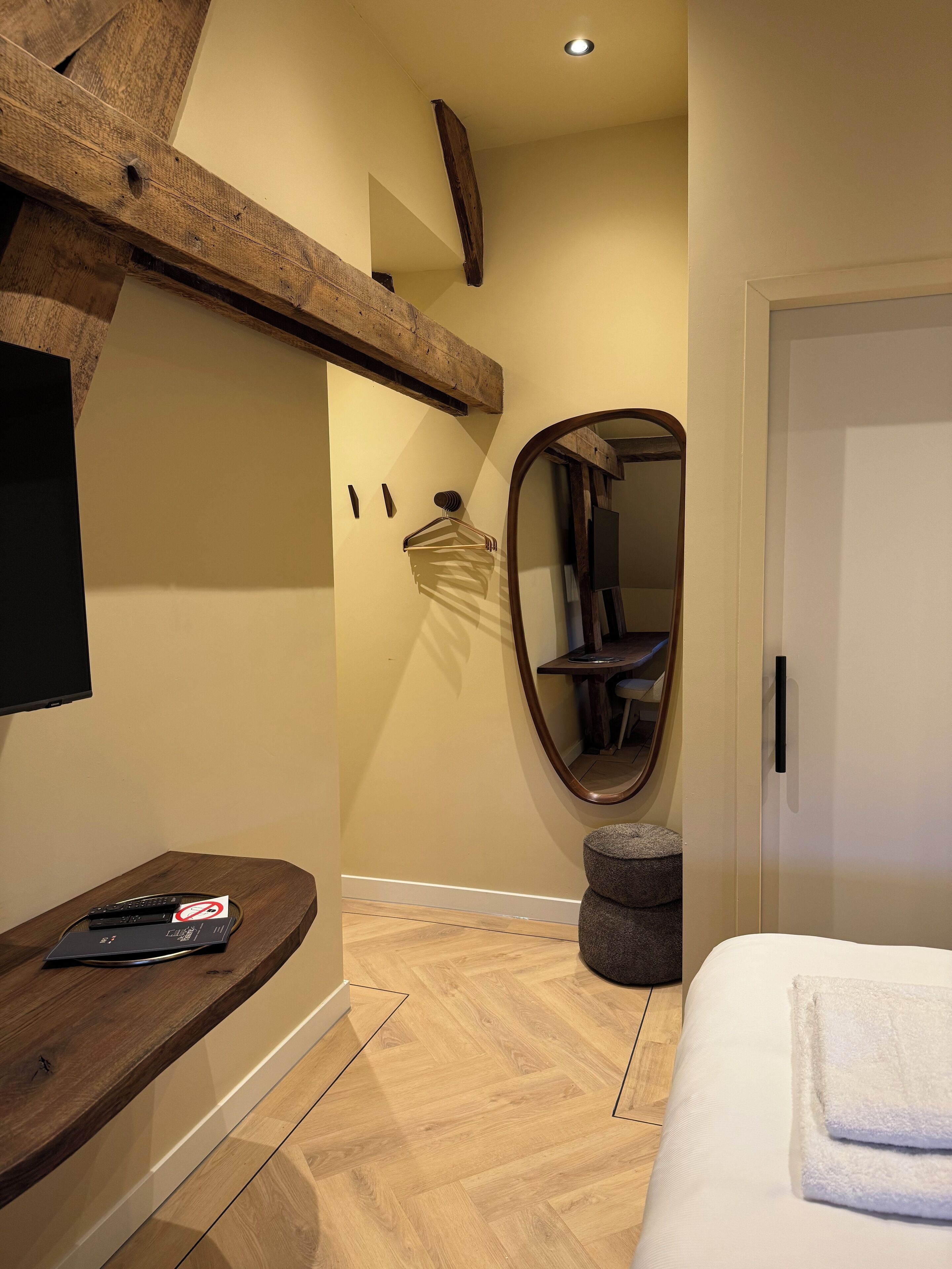 A bedroom with a wooden headboard, a bedside table with a remote control, a mirror, and a bed with a white towel.