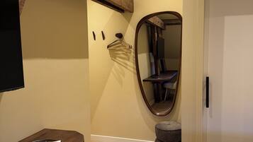 A bedroom with a wooden headboard, a bedside table with a remote control, a mirror, and a bed with a white towel.