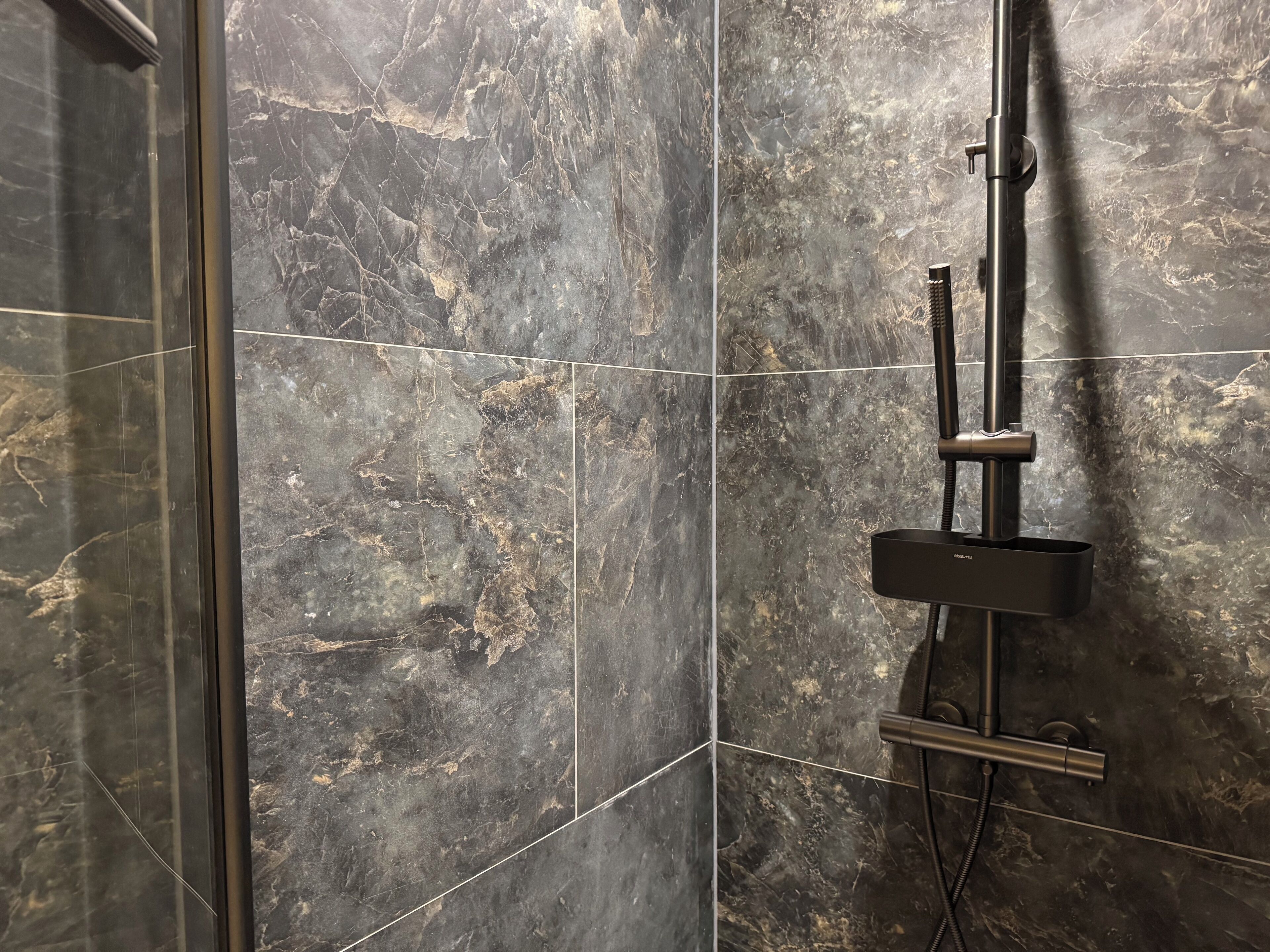 Un baño con baldosas de mármol oscuro y un sistema de ducha moderno.