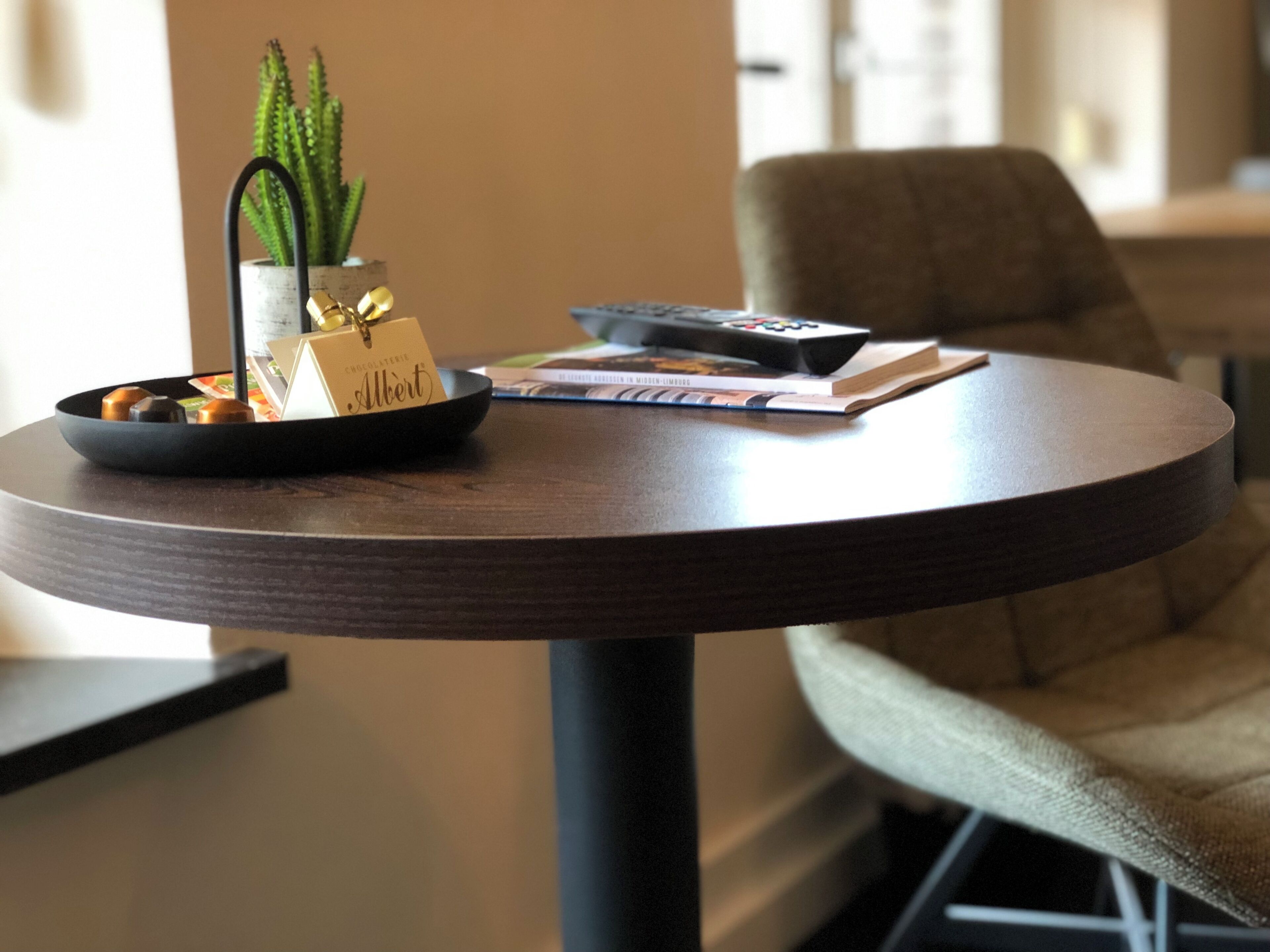 Une table ronde sur laquelle se trouvent un bol noir contenant une plante et des chocolats, une télécommande et un livre.
