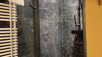 Un bagno moderno con doccia vetrata, portasciuga asciugamani bianco e soffione nero.