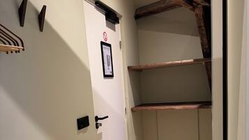 Um corredor estreito com teto de madeira, uma porta branca com placa de proibido fumar e uma estante de madeira.
