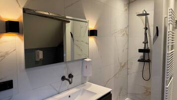 Une salle de bain moderne avec un lavabo blanc, un grand miroir, une douchette à main et un porte-serviettes.