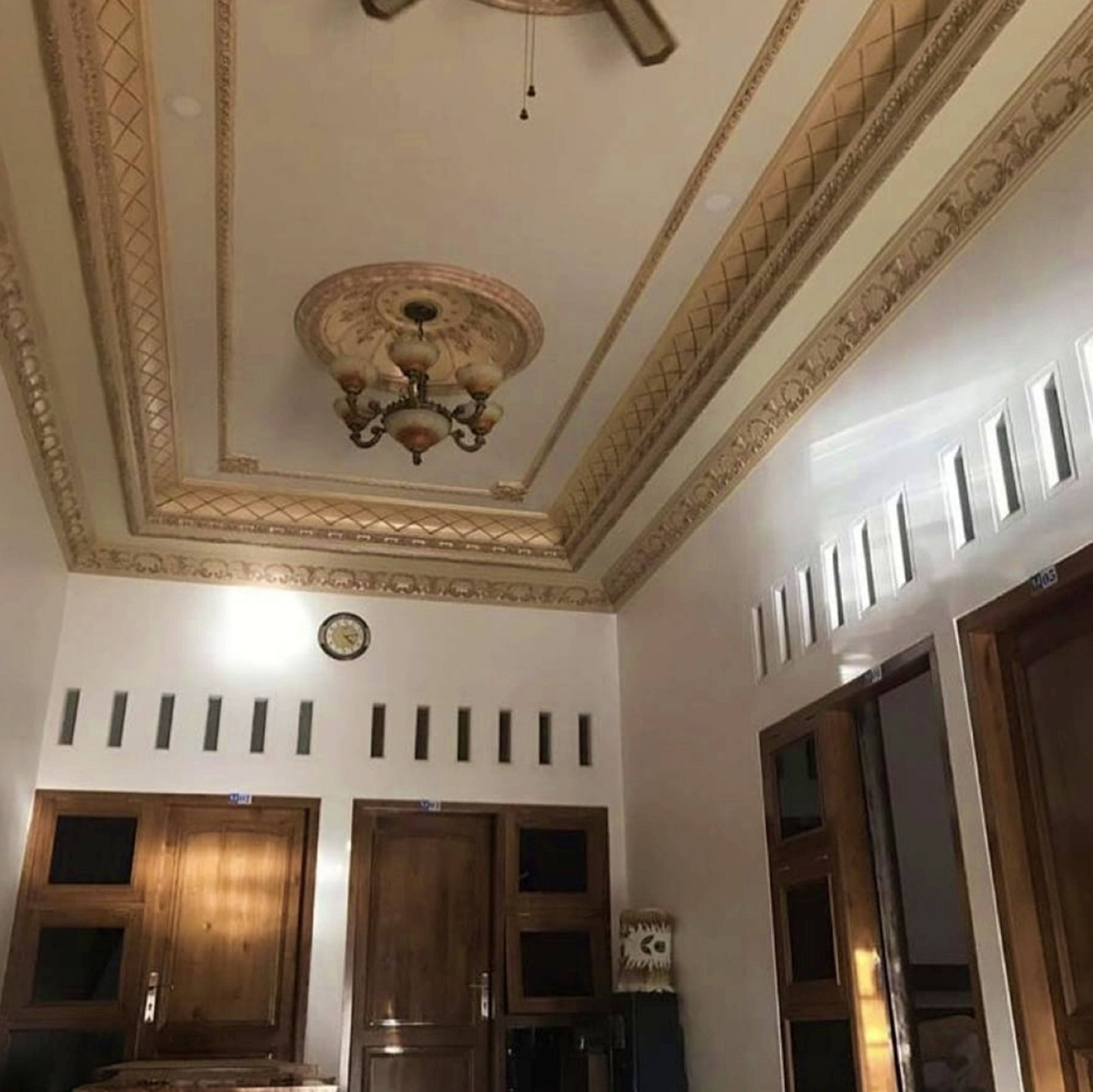 A room with a decorative ceiling, wooden doors, and a clock.