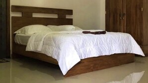Een slaapkamer met een houten bed, witte beddengoed en een houten garderobe.