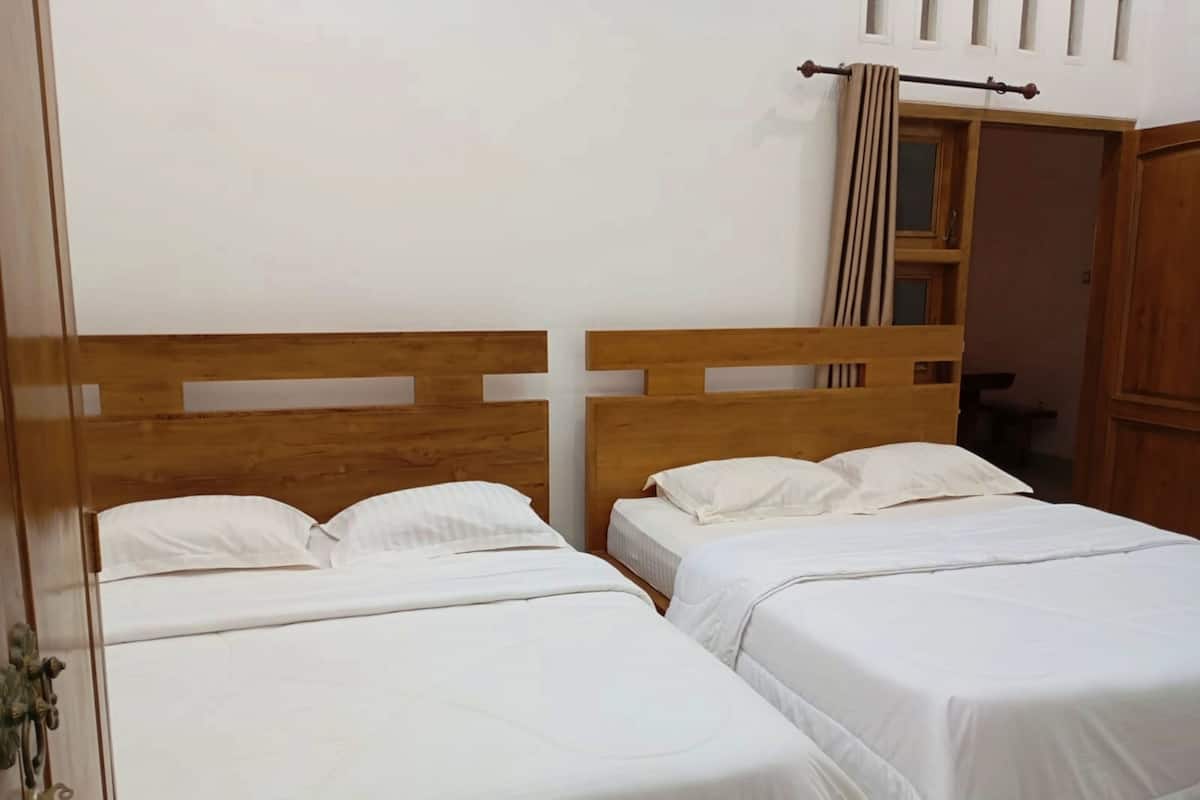 Een kamer met twee houten bedden, witte beddengoed en een houten hoofdbord, voorzien van een raam en gordijn.