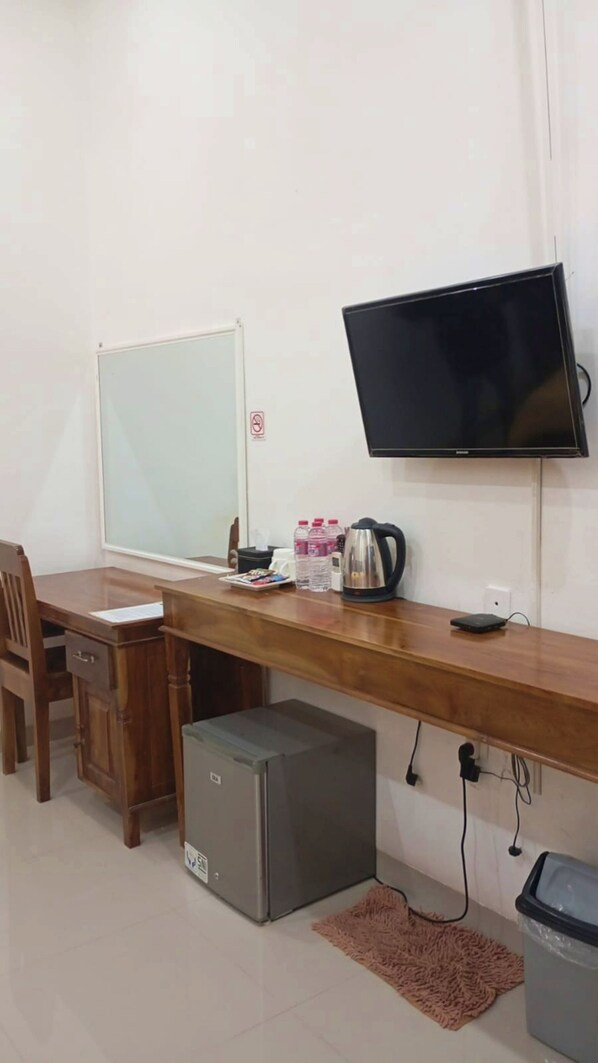 Un pequeño espacio de oficina con un escritorio, una silla, una pizarra, un televisor y un refrigerador.
