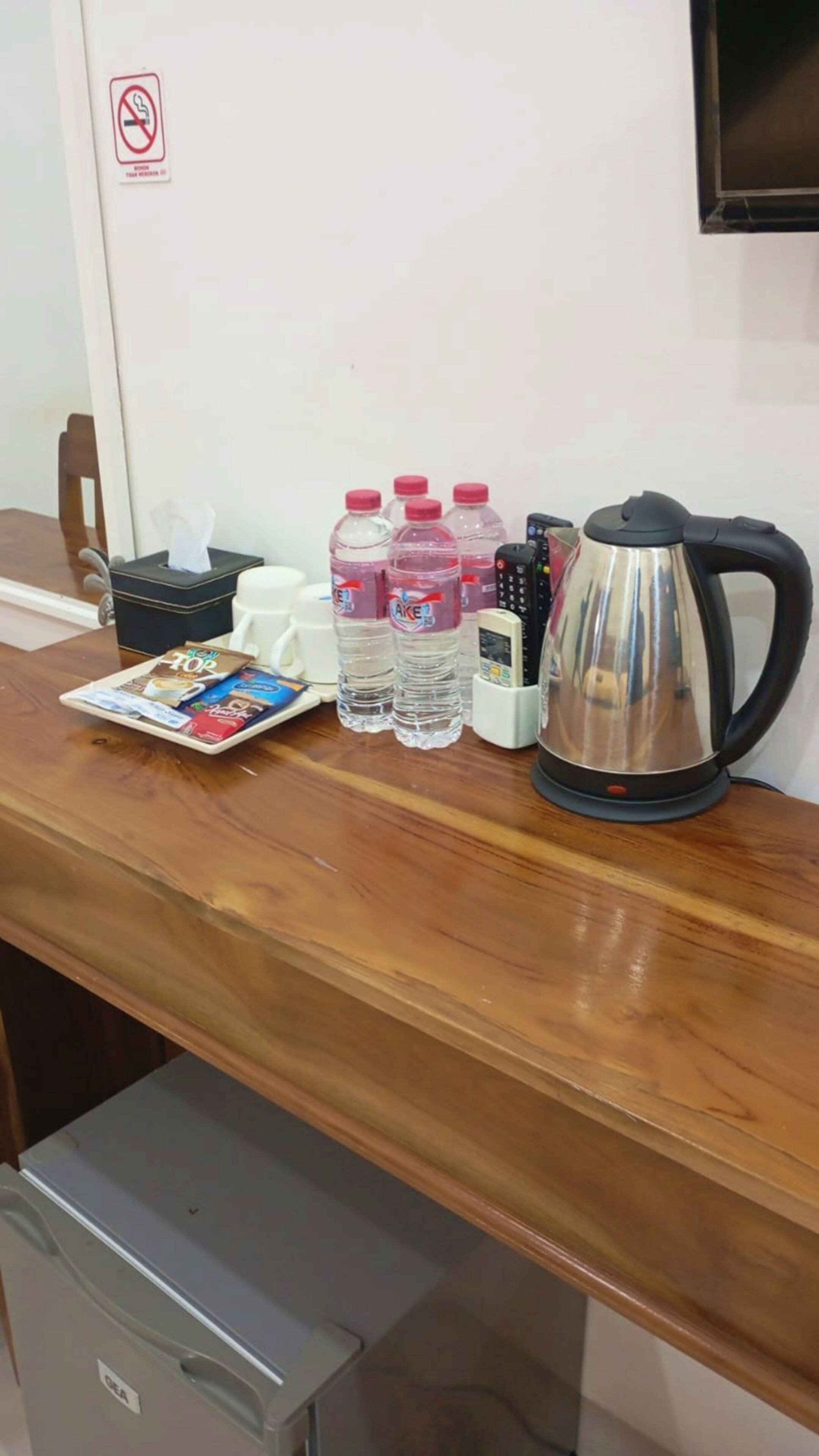Ein Holztisch mit Kaffeemaschine, Wasserflaschen, Taschentuchbox und Fernbedienung.