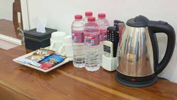 Un comptoir en bois avec une machine à café, des bouteilles d’eau, une boîte de mouchoirs et une télécommande.