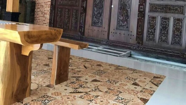 Een houten bank voor een grote, versierde deur met ingewikkelde houtsnijwerken.