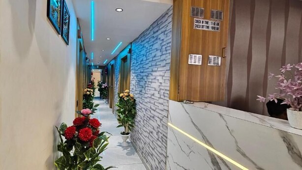Un pasillo de hotel con piso de mármol, plantas en macetas y una recepción con letrero de registro de entrada y salida.
