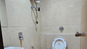 Un baño pequeño con inodoro, lavabo y ducha. Hay un cubo de basura y un calentador de agua en la pared.