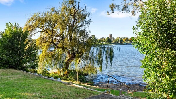 Ein Park mit einem See, einer Holzterrasse und einer Steintreppe, die zum Wasser hinabführt.