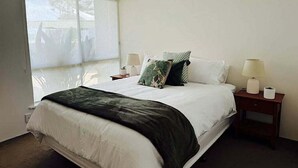 Ein Schlafzimmer mit einem großen Bett, zwei Nachttischen mit Lampen und einem Fenster mit Jalousien.