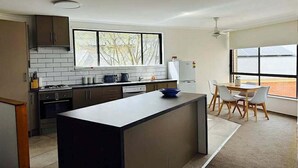 Eine moderne Küche mit einer zentralen Kochinsel, einem Essbereich mit Tisch und Stühlen sowie großen Fenstern, die für natürliches Licht sorgen.