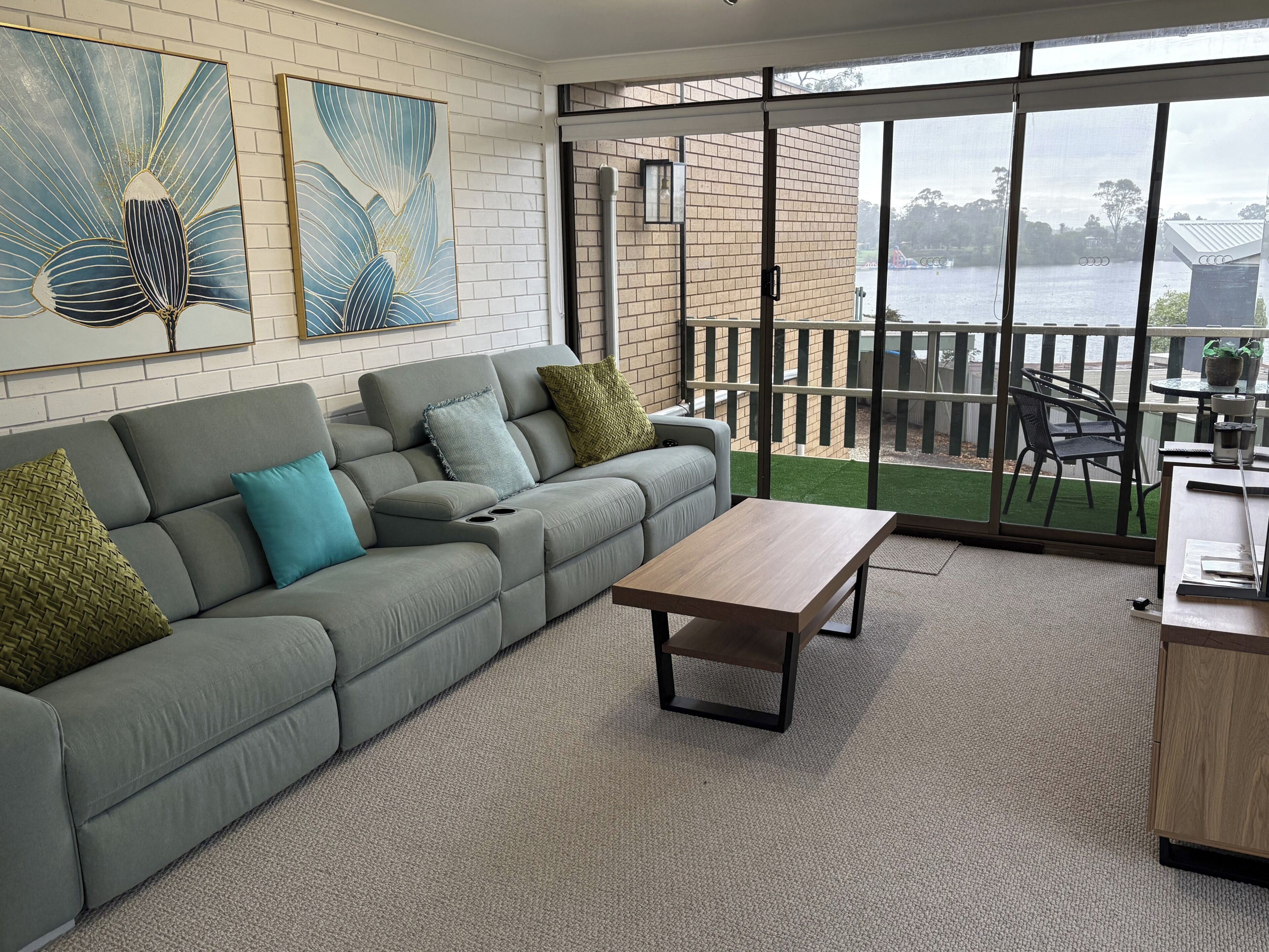 A modern living room with a grey sofa, a wooden coffee table, and a view of a lake through large windows.