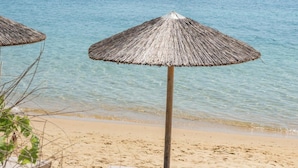 A beach with thatched umbrellas and lounge chairs, a sailboat in the background, and clear blue water. - Villa Delta Skiathos (Skiathos)