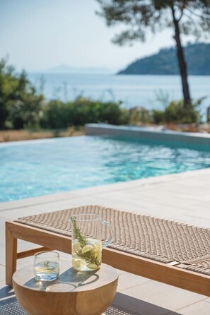 Un cadre agréable au bord de la piscine, avec une vue dégagée sur la mer et une montagne qui se profile à l’horizon.